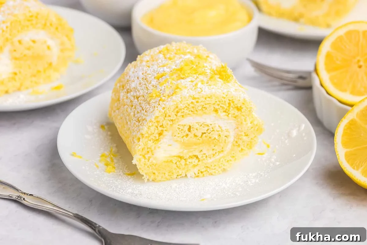 Zesty Lemon Swiss Roll Cake Recipe 2 A slice of lemon cake roll with cream filling, dusted with powdered sugar, sits on a white plate.
