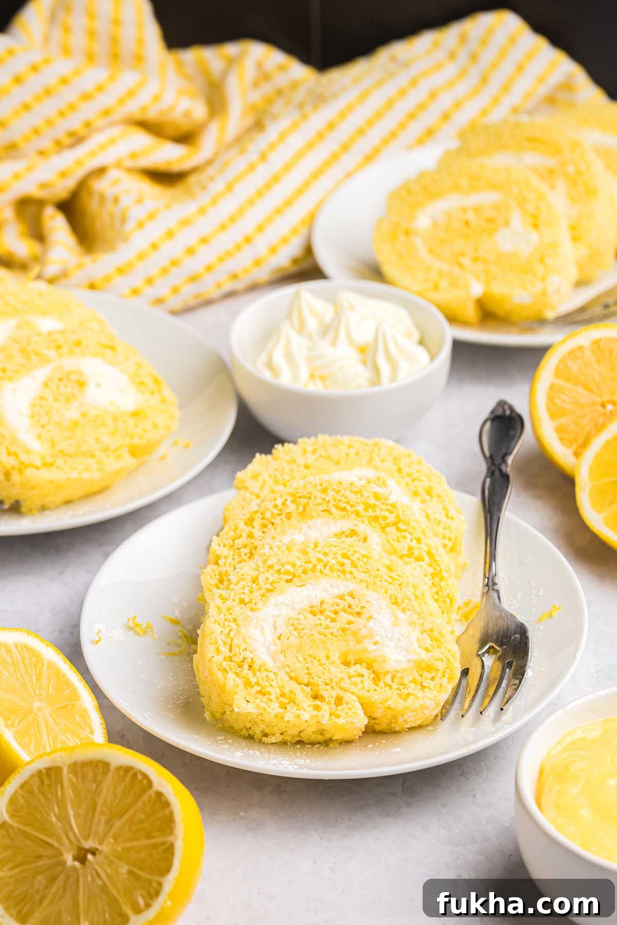Zesty Lemon Swiss Roll Cake Recipe 11 Slices of lemon cake roll on plates with cream and fresh lemons.