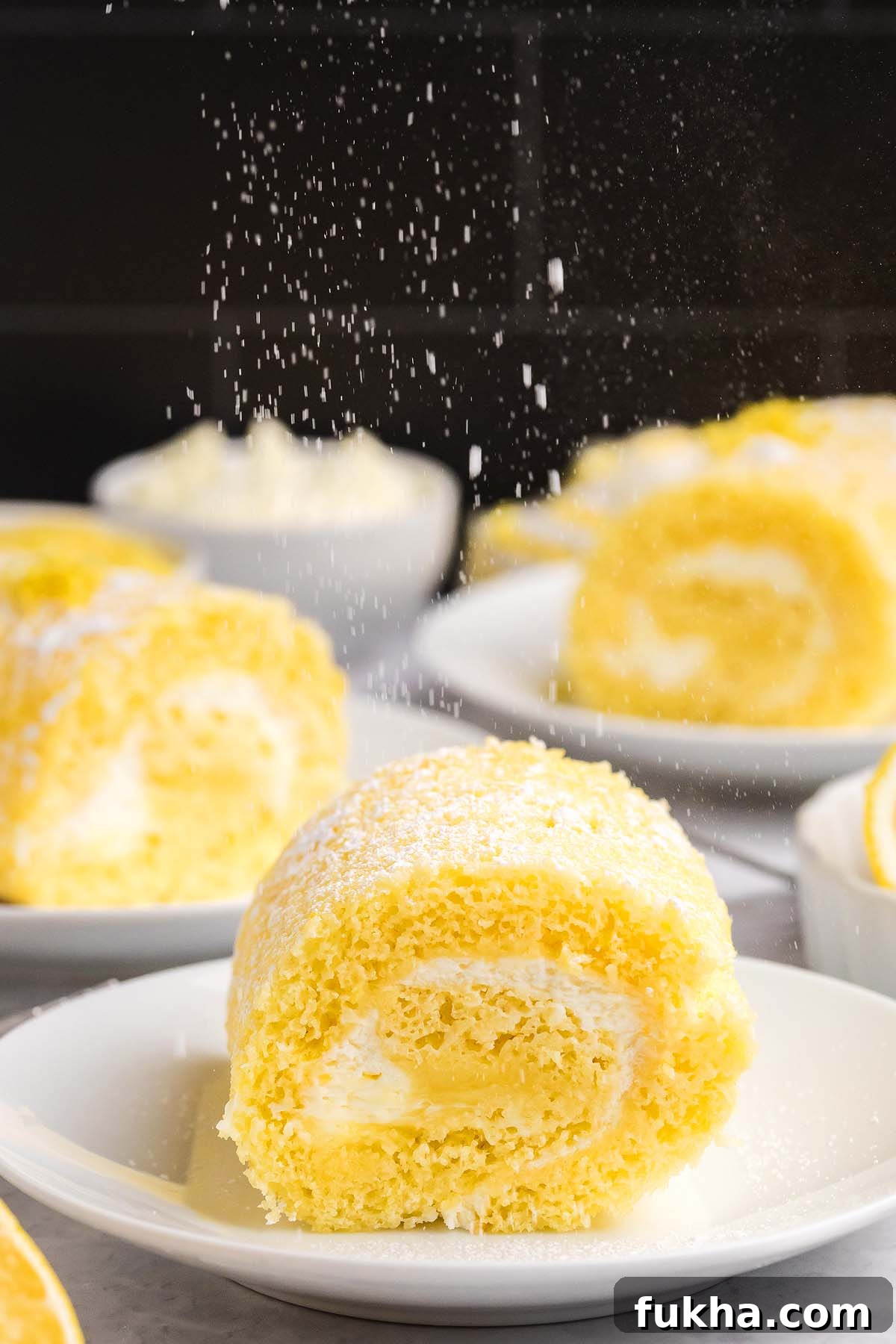 Zesty Lemon Swiss Roll Cake Recipe 12 A lemon swiss roll cake is being dusted with powdered sugar on a white plate.