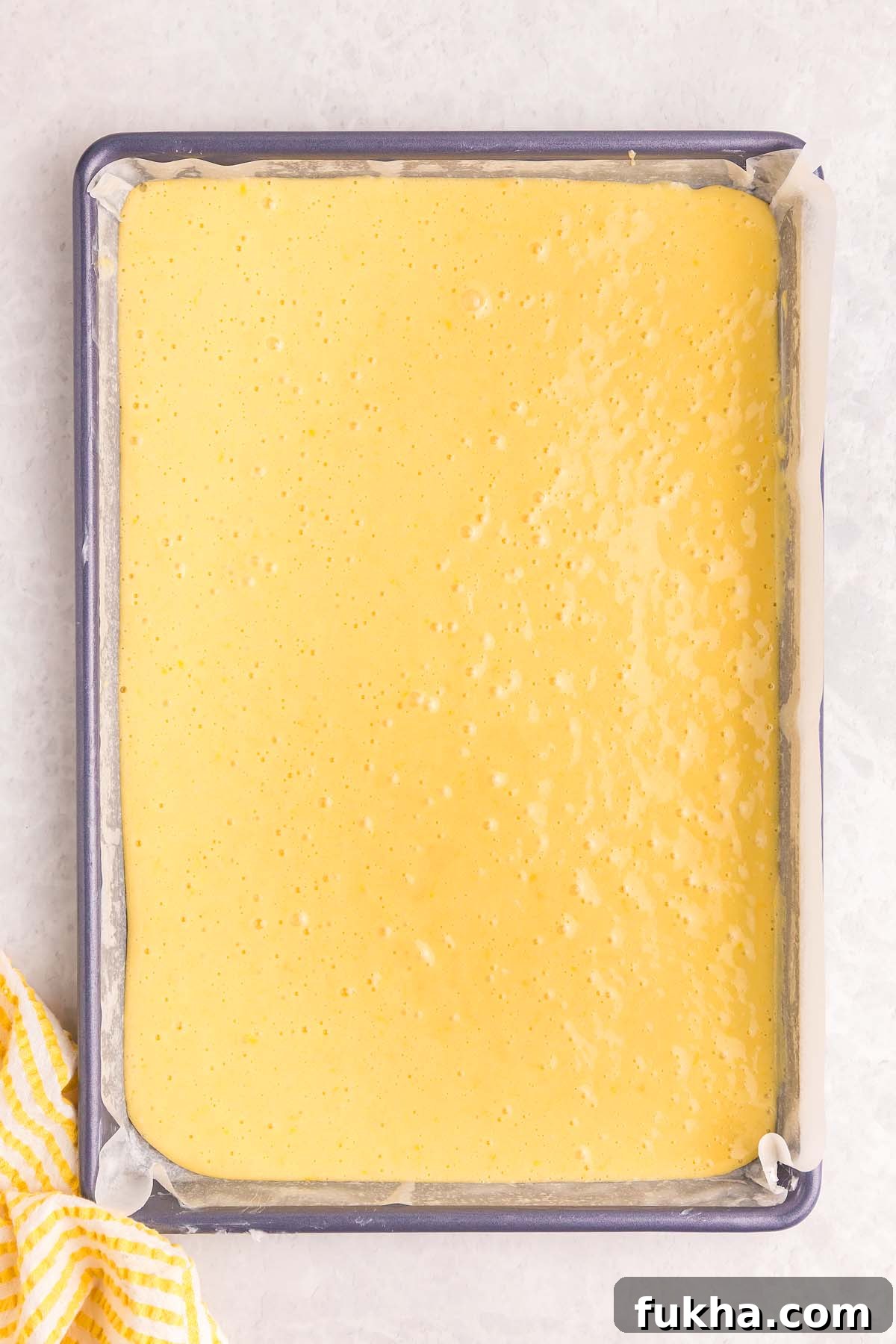 Zesty Lemon Swiss Roll Cake Recipe 15 A baking sheet filled with smooth yellow cake batter for a lemon roll cake, lined with parchment paper.
