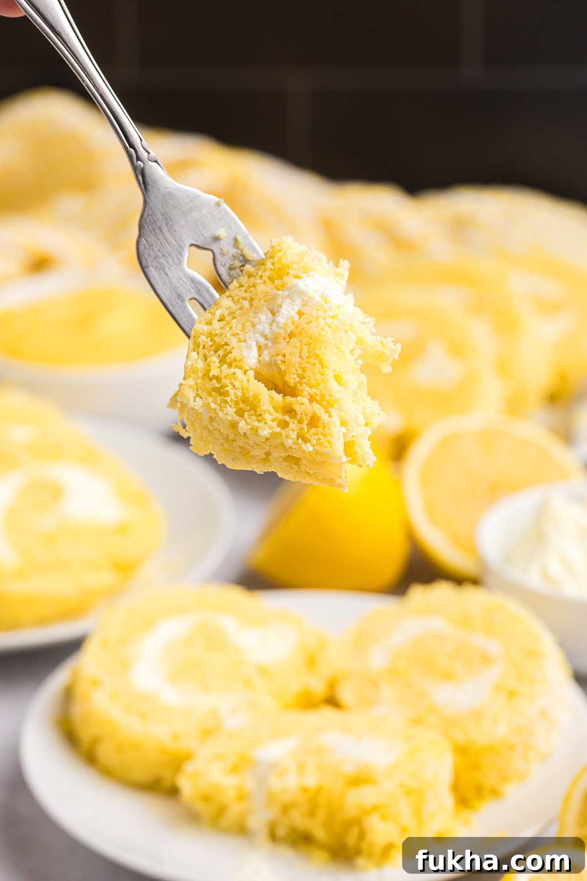 Zesty Lemon Swiss Roll Cake Recipe 5 A fork holds a bite of lemon swiss roll cake with creamy filling; more slices and fresh lemons are in the background.