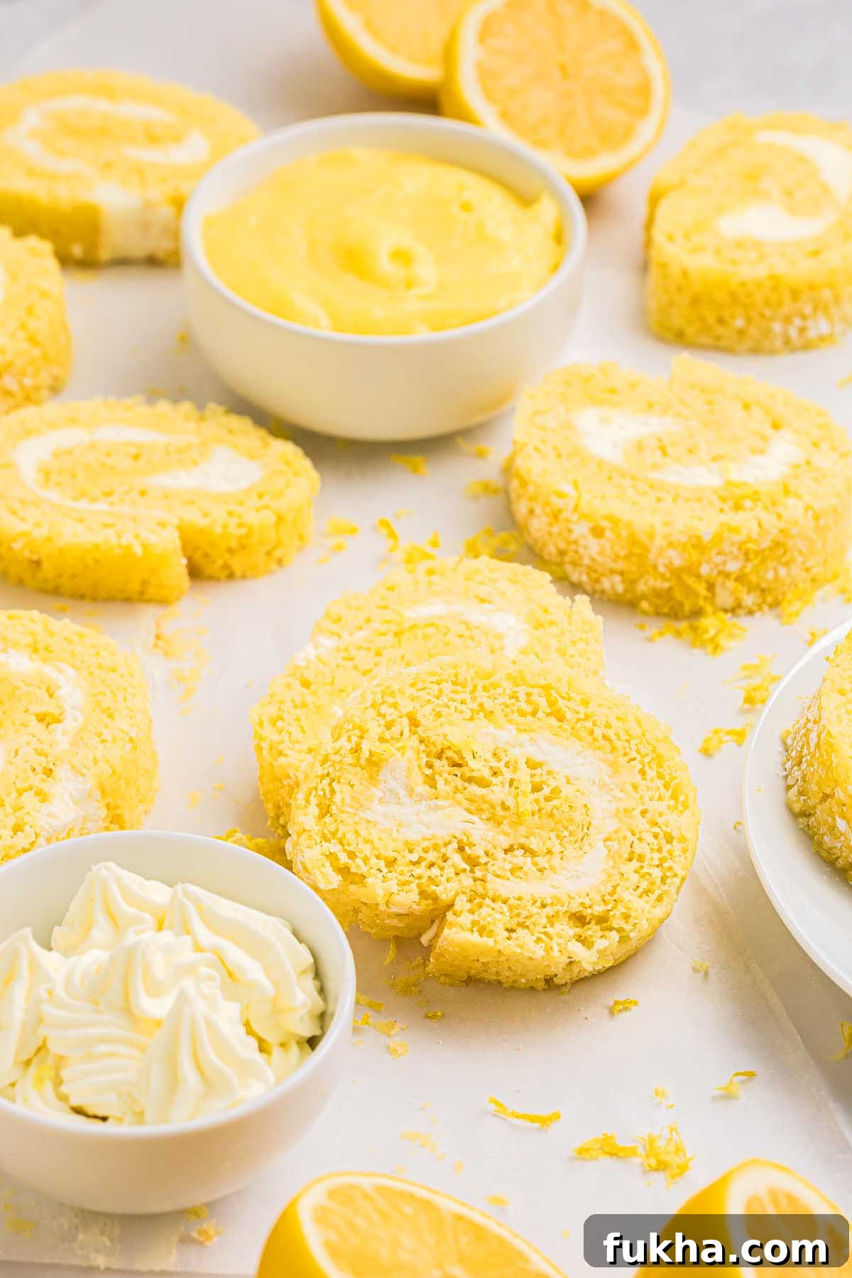 Zesty Lemon Swiss Roll Cake Recipe 8 Slices of lemon roll cake with cream filling, surrounded by lemons and bowls of lemon curd.
