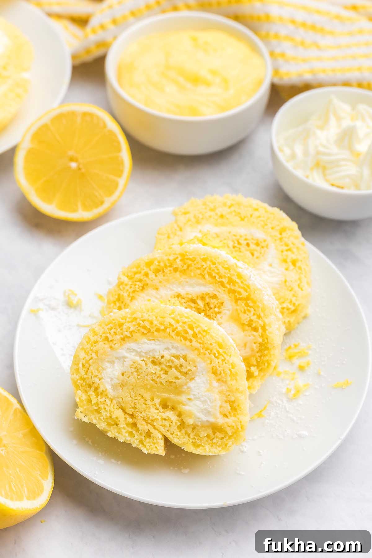 Zesty Lemon Swiss Roll Cake Recipe 9 Three slices of lemon Swiss roll cake with cream filling rest on a white plate, surrounded by lemons and bowls.