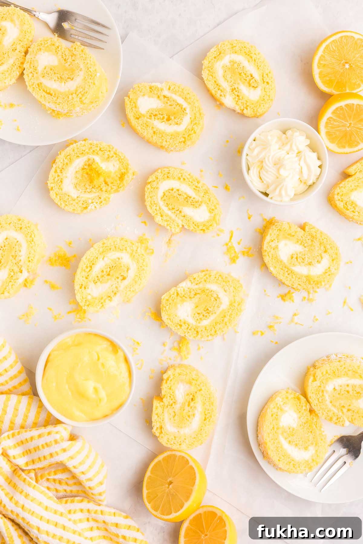 Zesty Lemon Swiss Roll Cake Recipe 10 Lemon swiss roll slices with cream filling, lemon cream, and halved lemons on a white surface.