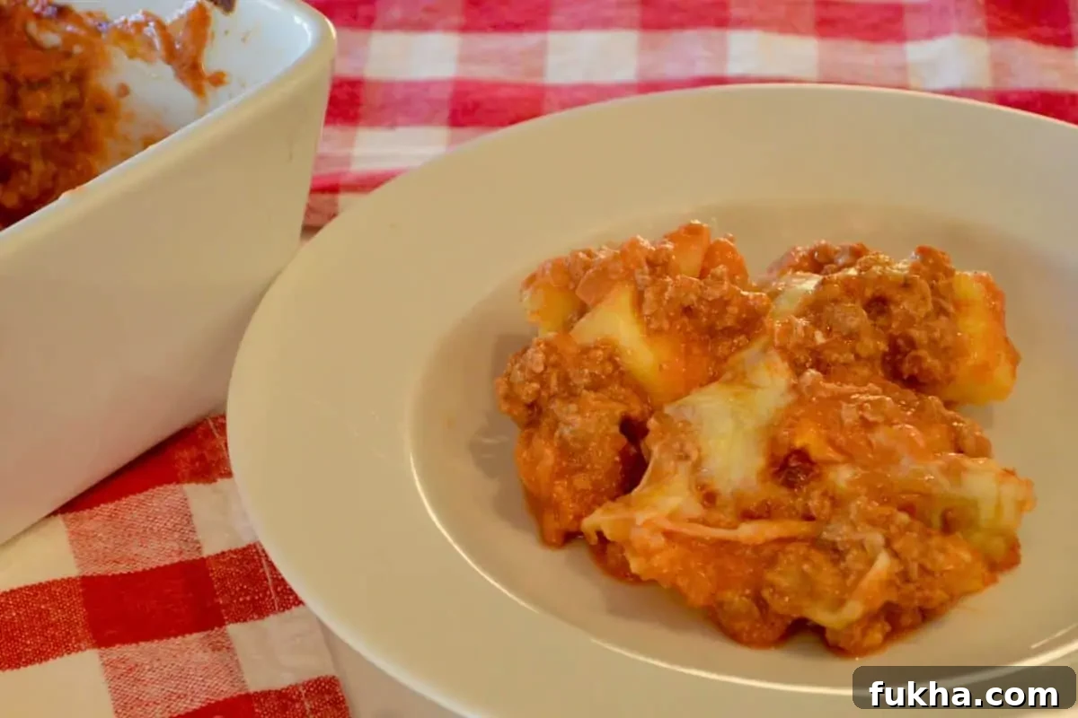 Cheesy Baked Tortellini Casserole with Meat Sauce 3 Baked tortellini casserole serving in a white bowl on a checkered napkin.