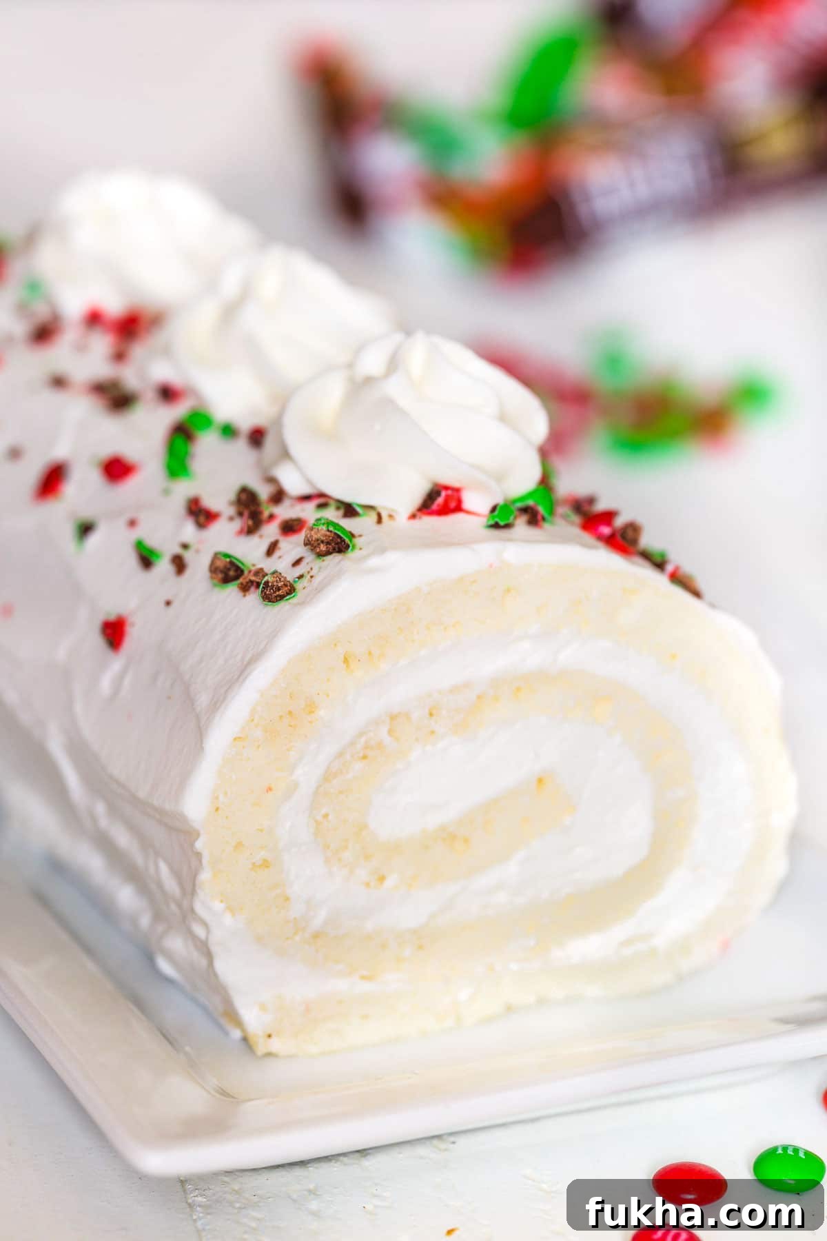 Snow White Roll Cake Recipe with Whipped Cream Filling 2 White roll cake topped with crushed red and green M&Ms.