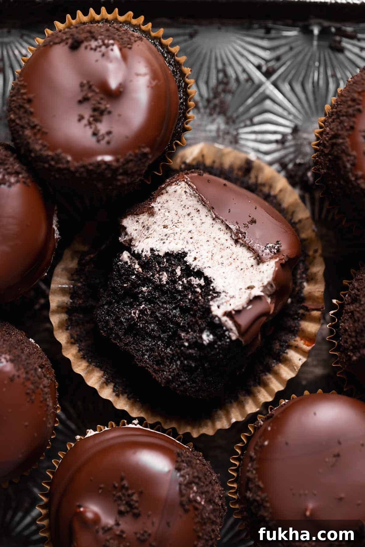 Chocolate oreo cupcakes on a baking tray with the center one missing a bite.