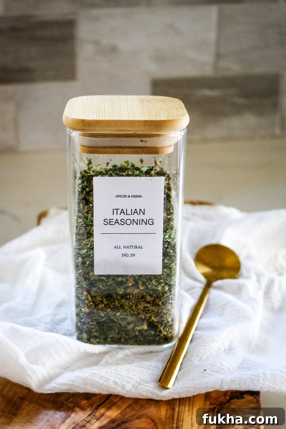 Italian seasoning in a transparent jar, with a spoon next to it.