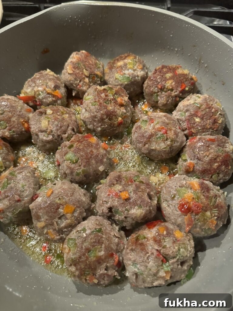 The raw Italian meatballs cooking in a skillet