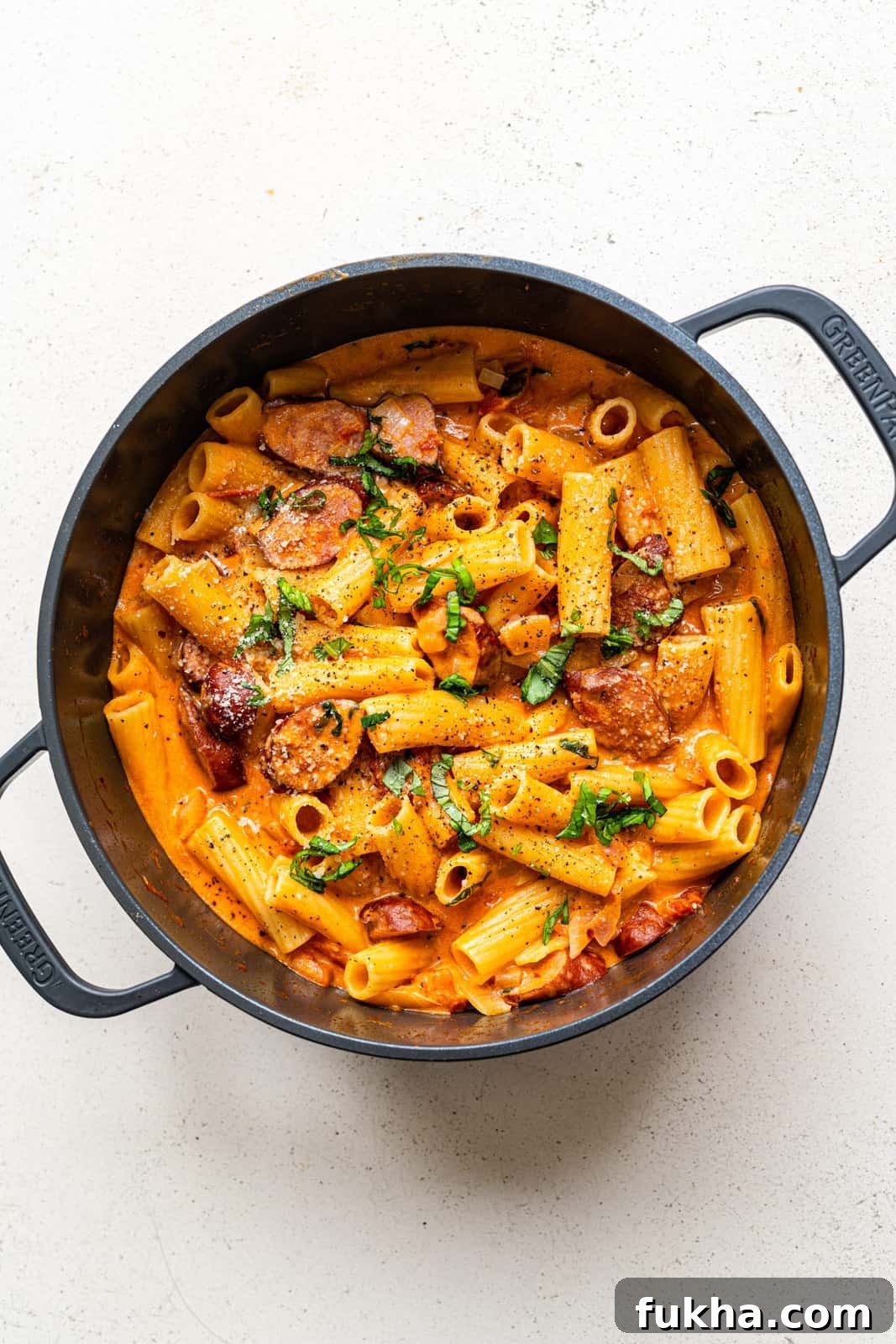 Pot of spicy sausage pasta in tomato and mascarpone sauce garnished with fresh chopped basil