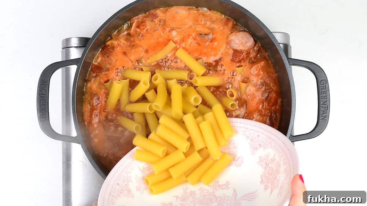 Cooking rigatoni pasta in a pot of tomato sauce and stock