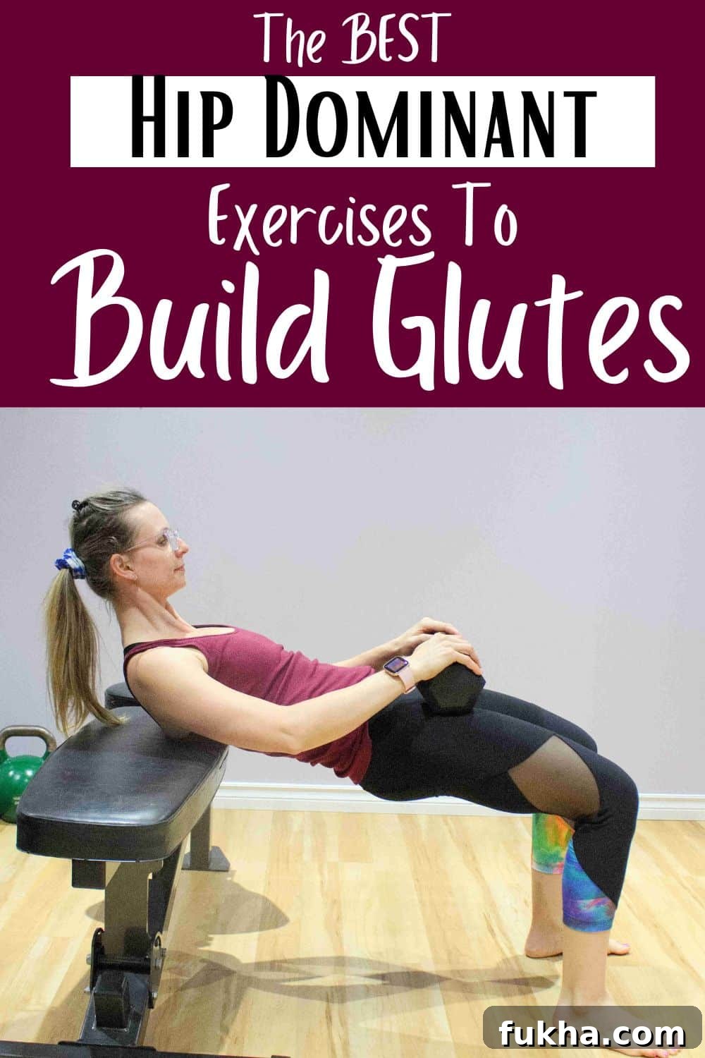 Woman in maroon shirt and black tights performing a hip thrust off a workout bench with a dumbbell in her lap.