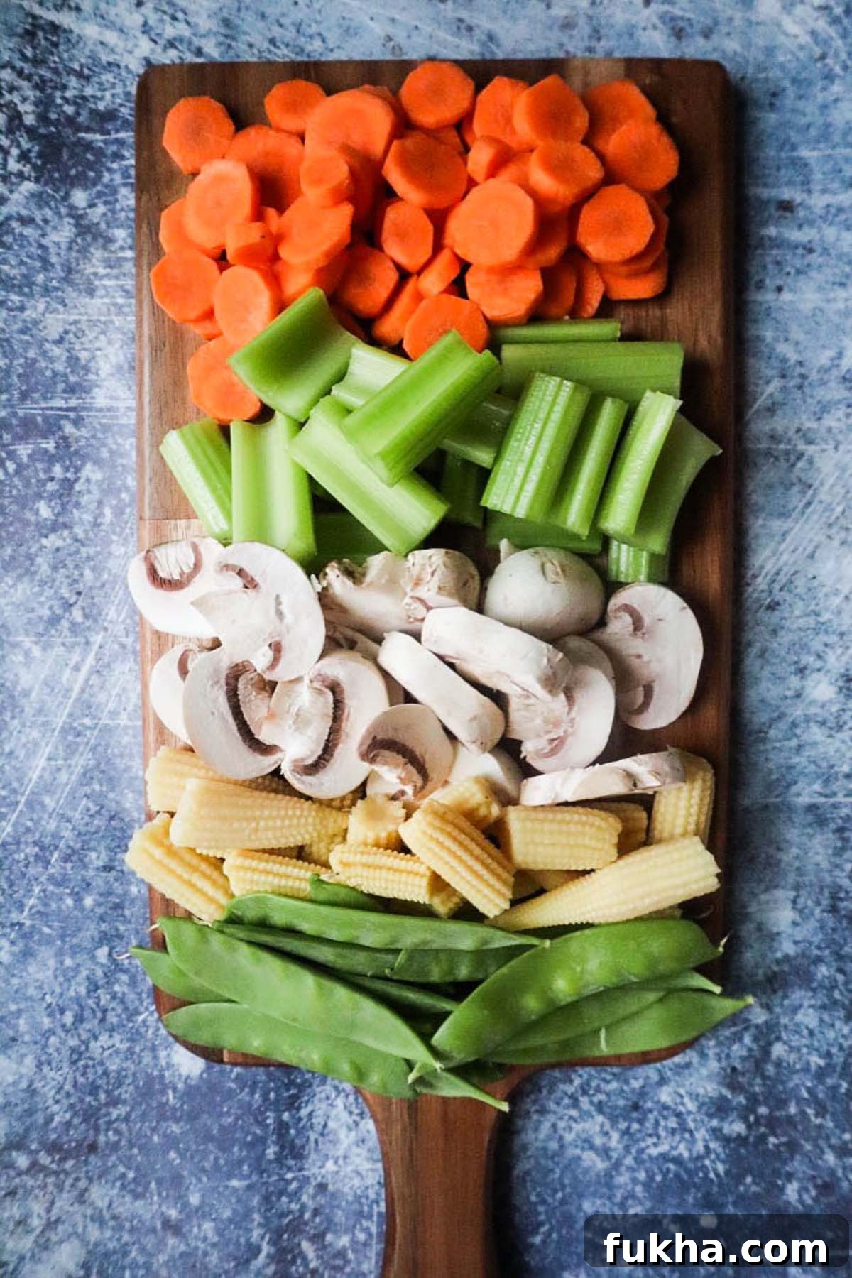 wooden cutting board with chopped vegetables including mushrooms, carrots, celery, and peas