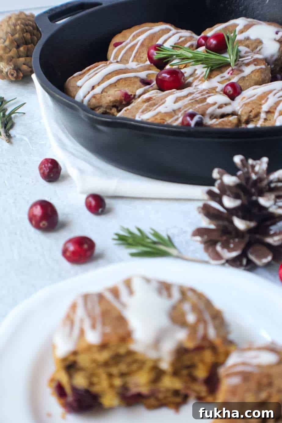 cranberry buttermilk biscuits topped with powdered sugar glaze in cast iron skillet garnished with fresh cranberries