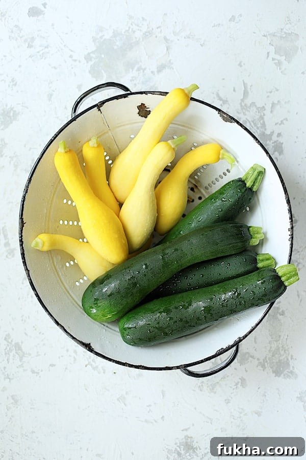 Photo of zucchini and yellow squash in white colander on white background.