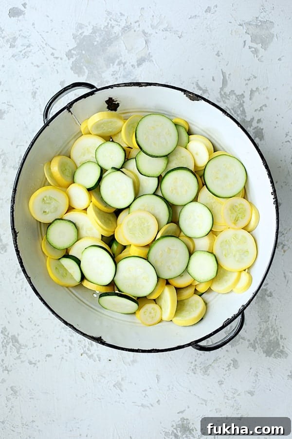 Photo of sliced zucchini and yellow squash in white colander on white background.
