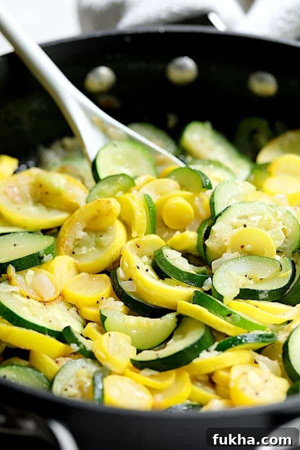 Photo of zucchini and yellow squash being sauteed in skillet with white spoon.