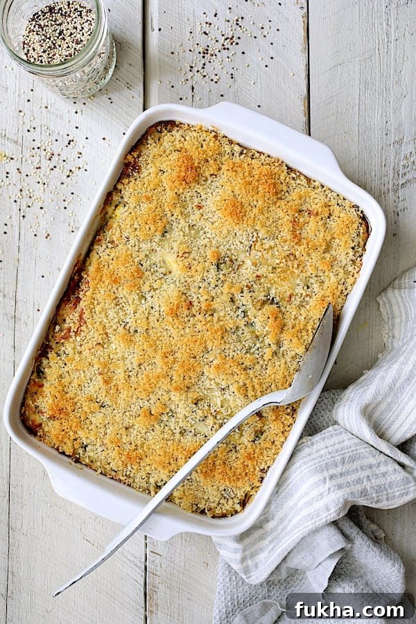 Photo of baked Zucchini, Yellow Squash and Quinoa Casserole on white wood background with white serving spoon and quinoa scattered about.
