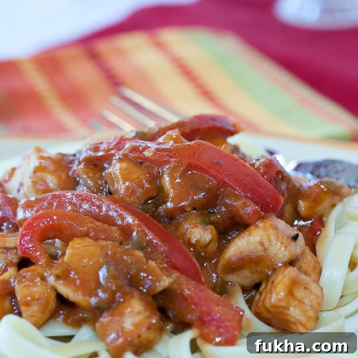 White plate with brown rim and fork with diced chicken, fettuccine, and sliced red bell pepper in a peanut sauce