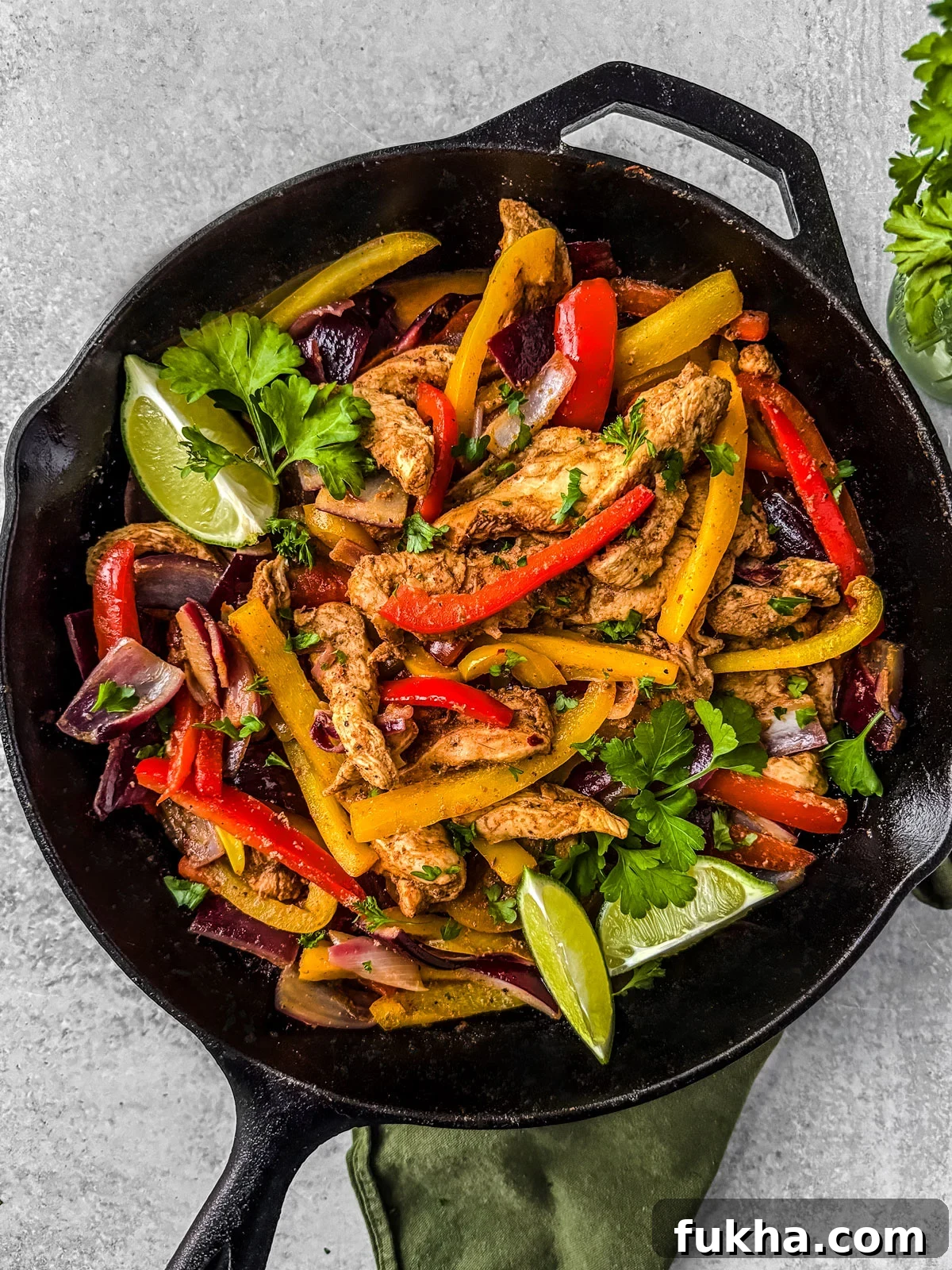 Skillet full of chicken and veggies with lime wedges.