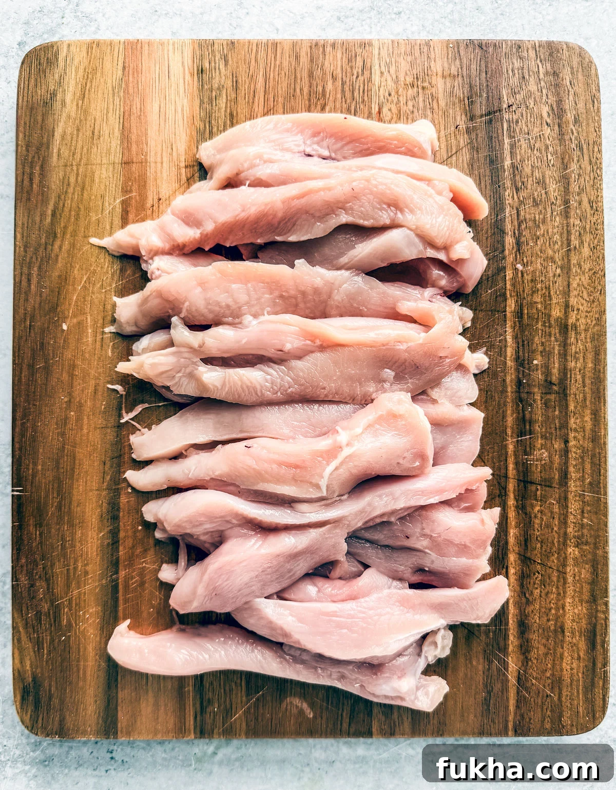 Chicken breasts cut into strips on a cutting board.