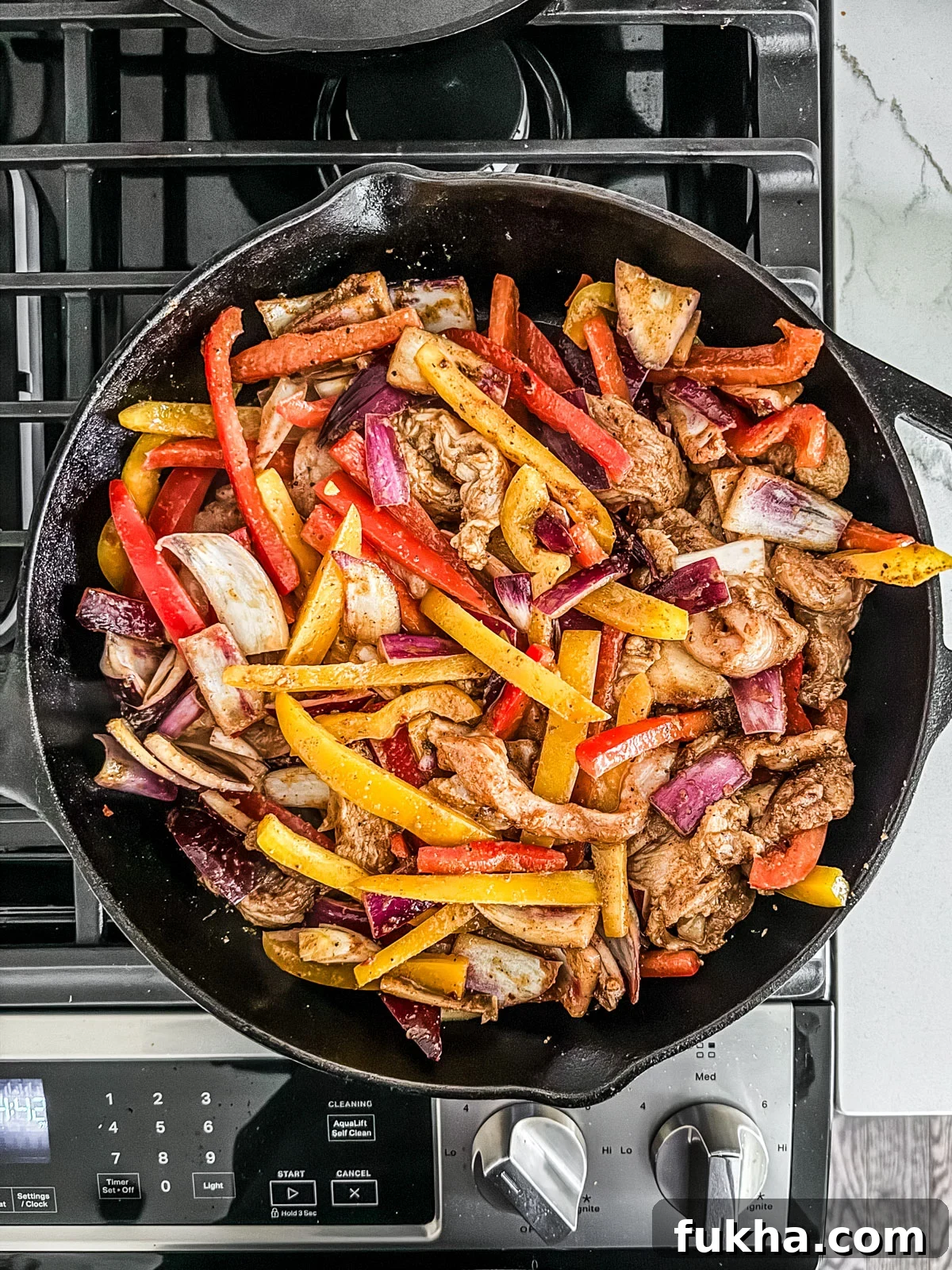 Skillet on stovetop with chicken strips, peppers, and onions.