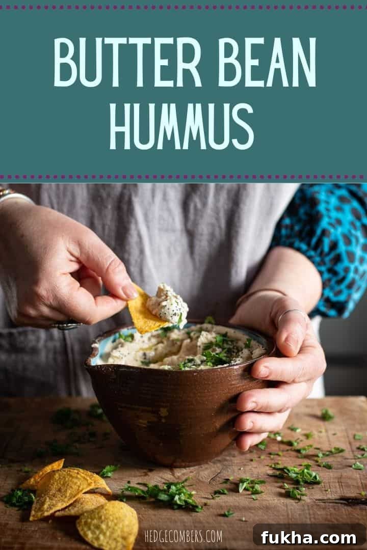 Womans hands scooping butter bean dip from a brown bowl on a wooden kitchen counter