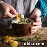 Womans hands scooping butter bean dip from a brown bowl on a wooden kitchen counter