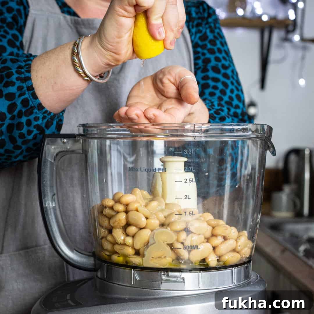 Woman in grey squeezing a lemon into a mixer of hummus ingredients