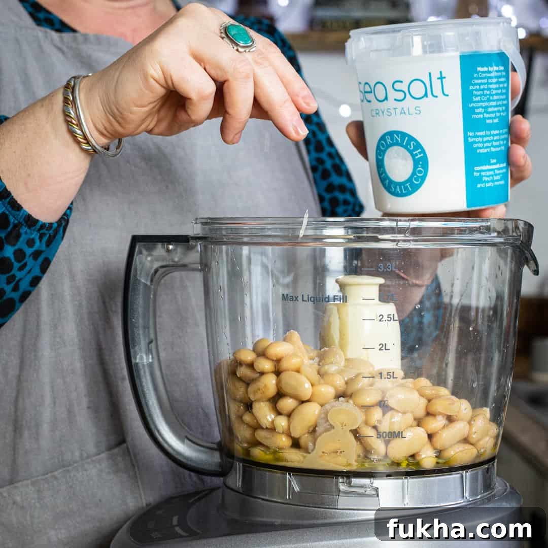 Woman sprinkling salt into a mixer of hummus ingredients
