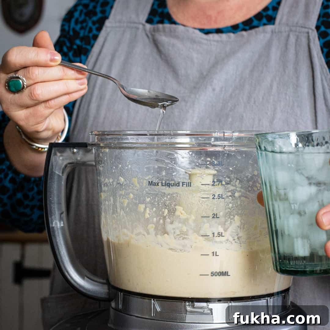 Woman in grey spooning ice water from a glass into a food processor
