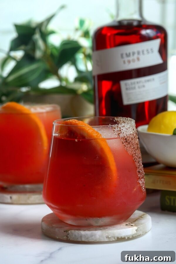 Prickly pear cocktail made with empress gin, with a spicy sugar Rim and a blood orange for garnish.