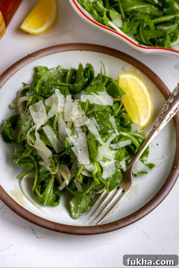 An arugula fennel salad with a delicious honey dijon dressing with a lemon on the side and fork in the plate.
