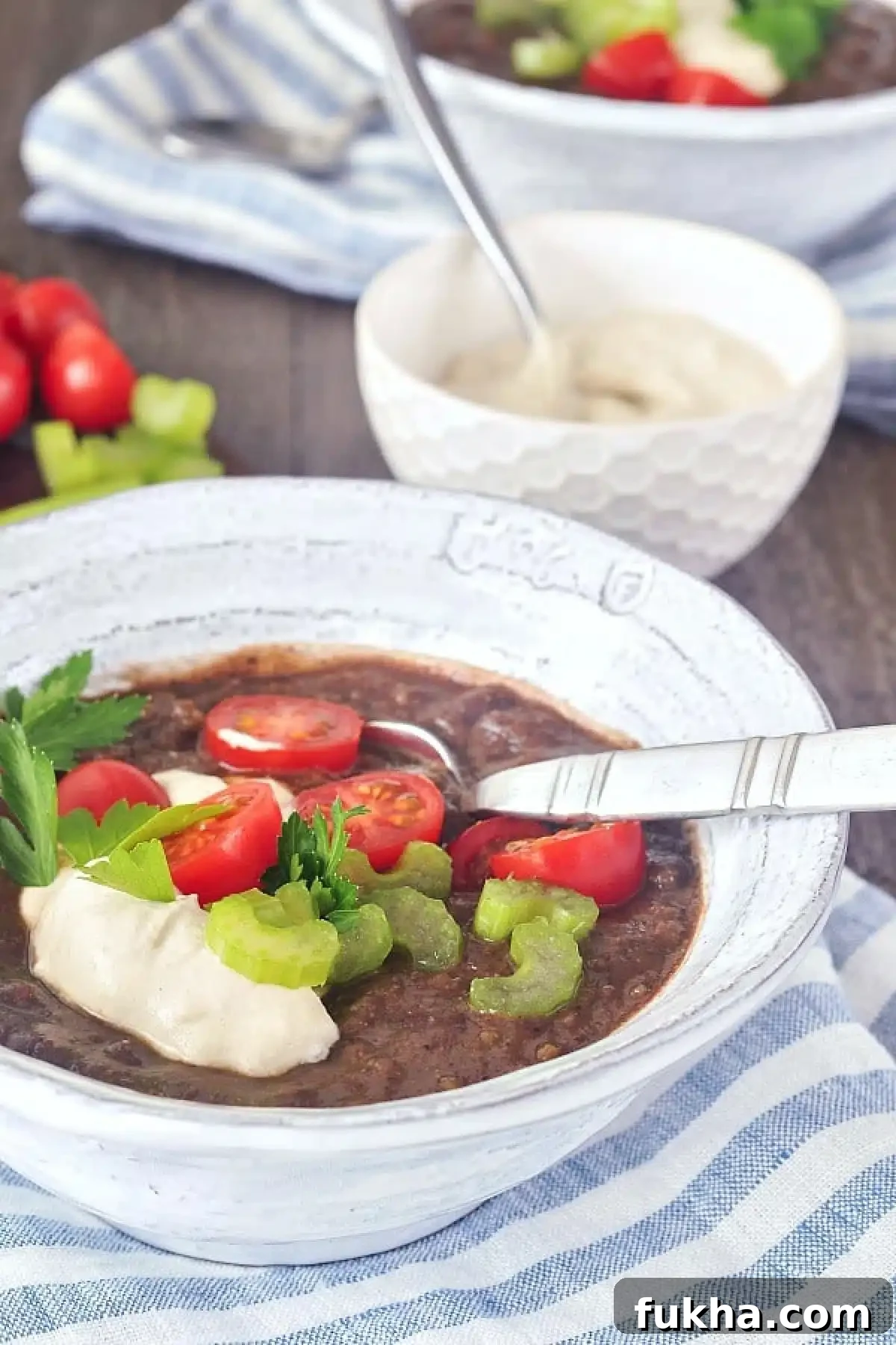 Chipotle Black Bean Soup in bowls, garnished with cherry tomatoes, cashew cream, and green parsley.