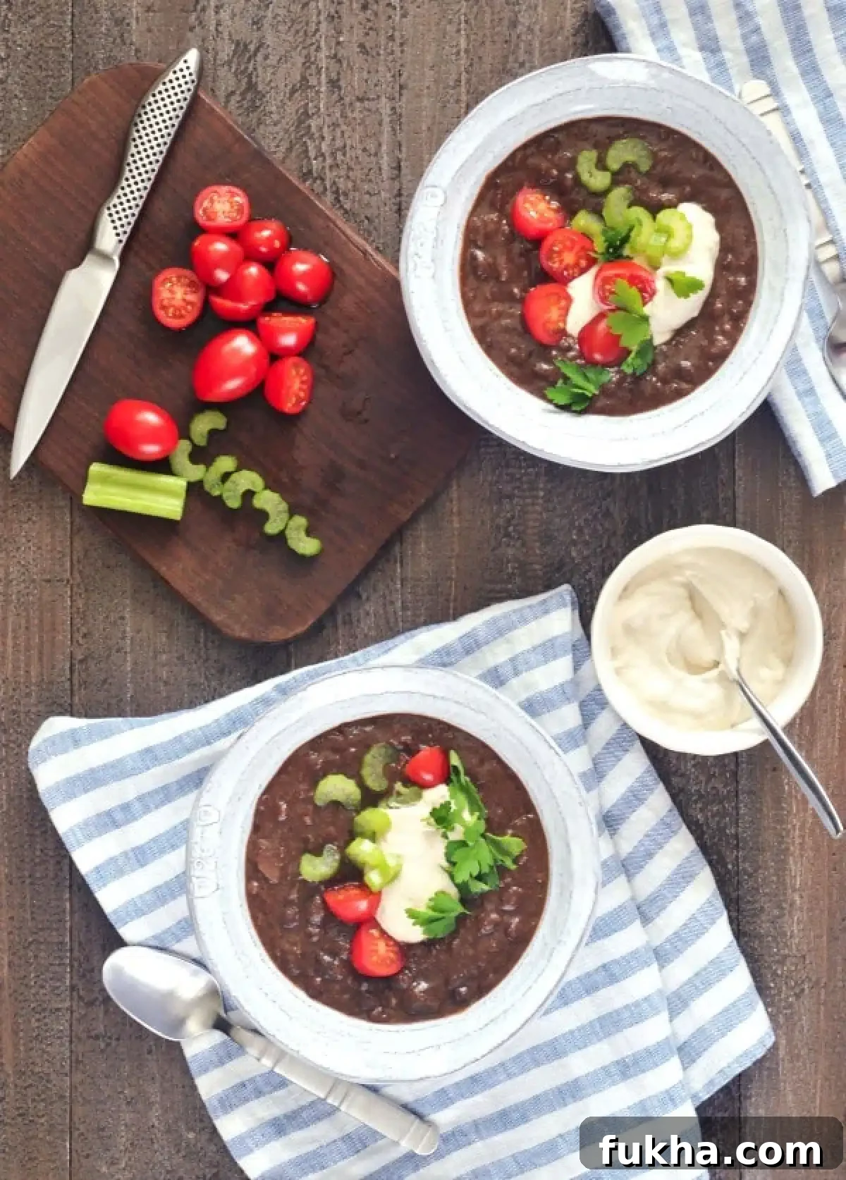 Overhead view of Chipotle Black Bean Soup in bowls, garnished with cherry tomatoes, cashew cream, and green parsley.
