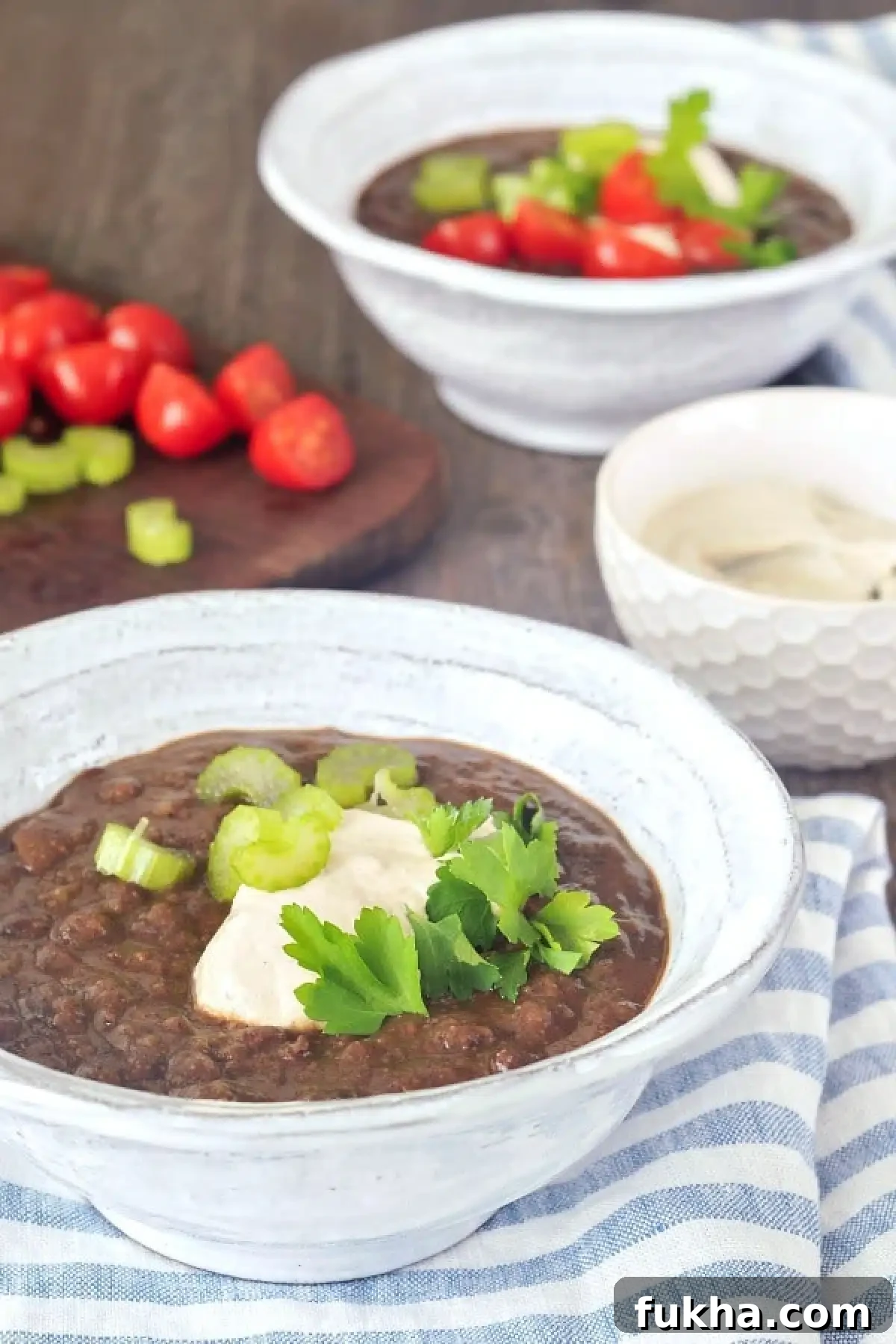 Chipotle Black Bean Soup in bowls, garnished with cherry tomatoes, cashew cream, and green parsley.
