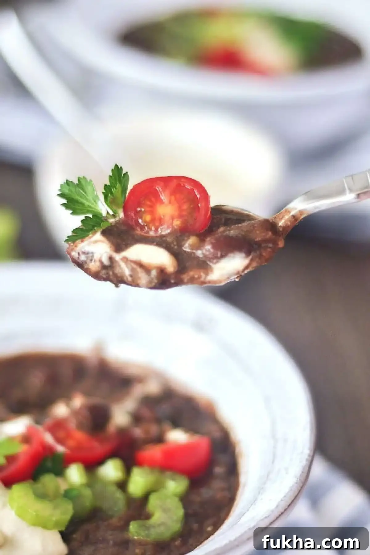closeup of a spoonful of Chipotle Black Bean Soup with a tomato and parsley leaf garnish.