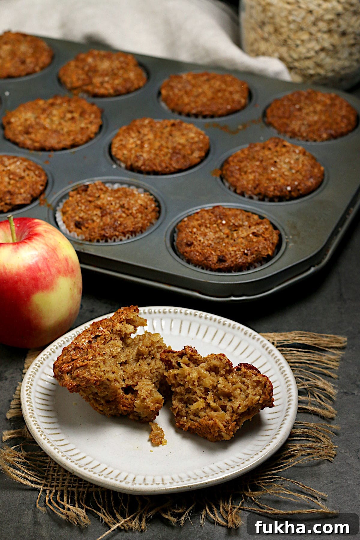 An Apple Cinnamon Oatmeal Muffin broken in half on a small white plate.