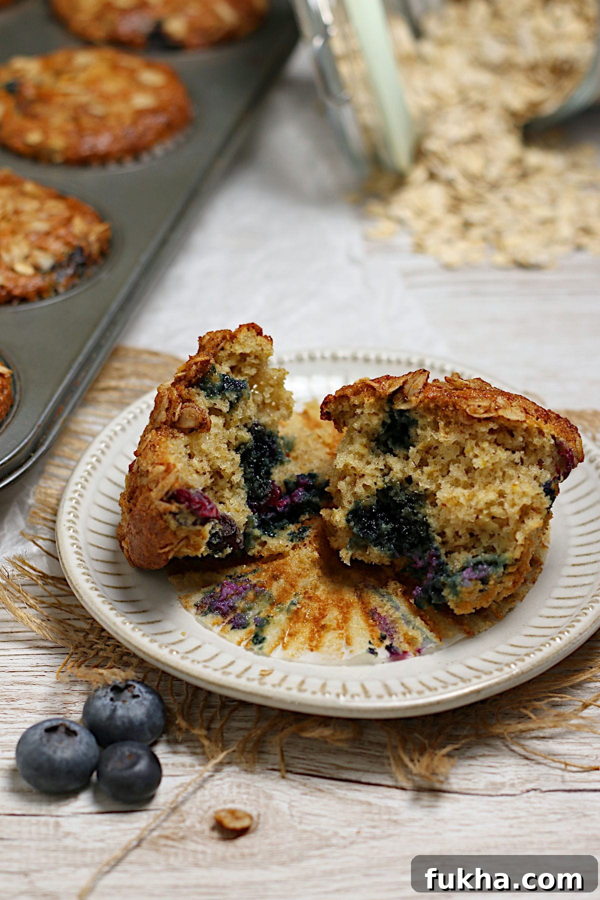 A blueberry oatmeal muffin broken into two pieces on a small white plate.