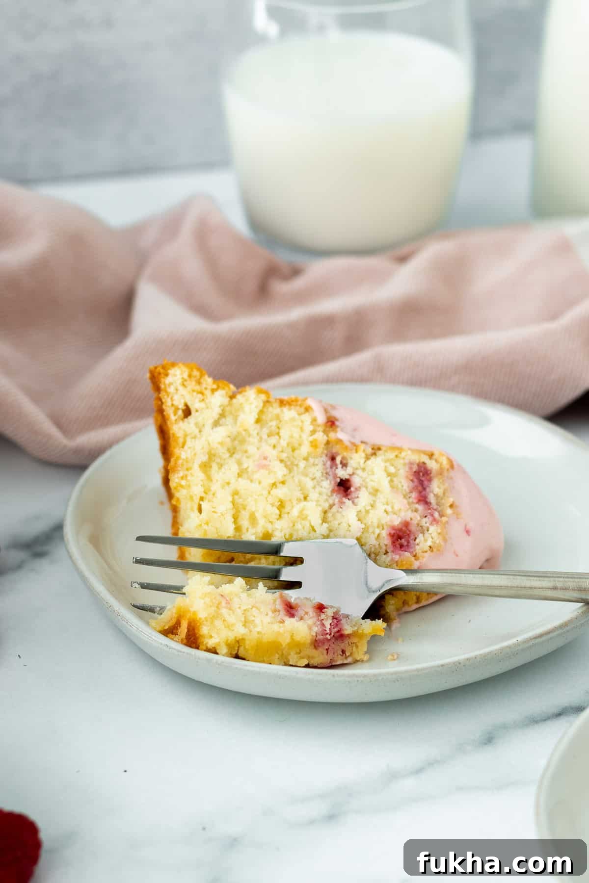 Decadent White Chocolate Raspberry Bundt Cake Recipe 5 slice of white chocolate raspberry bundt cake on a gray plate with pink linen