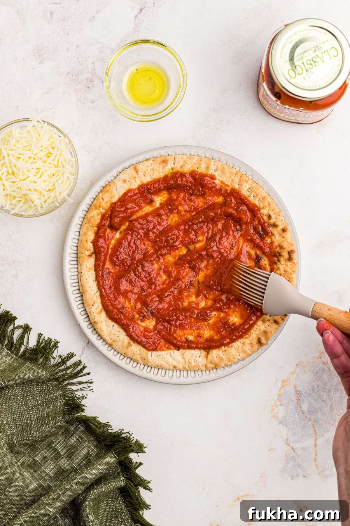 Make Crispy Air Fryer Pita Pizzas in 10 Minutes 4 Pizza sauce being brushed over a slice of pita bread on a marble table.