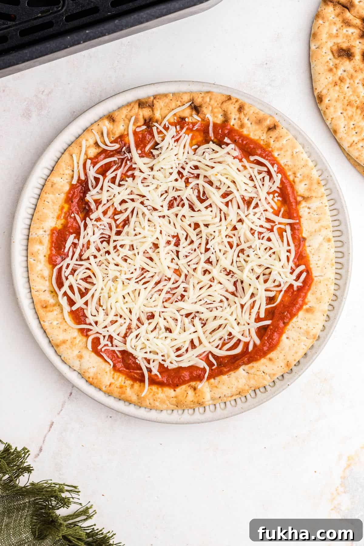 Make Crispy Air Fryer Pita Pizzas in 10 Minutes 5 Sauce and shredded cheese on pita bread before cooking in the air fryer basket.