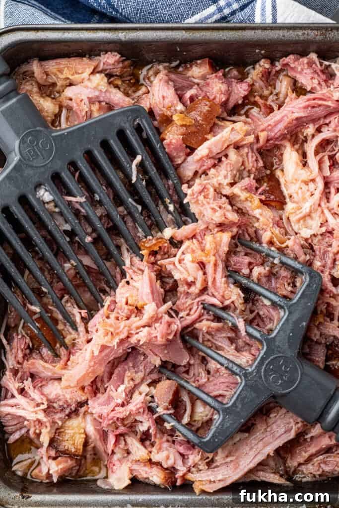 Shredding Pulled Pork Ham in pan with large meat shredders