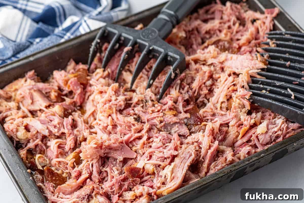 Smoked pulled ham in shallow baking dish being shredded
