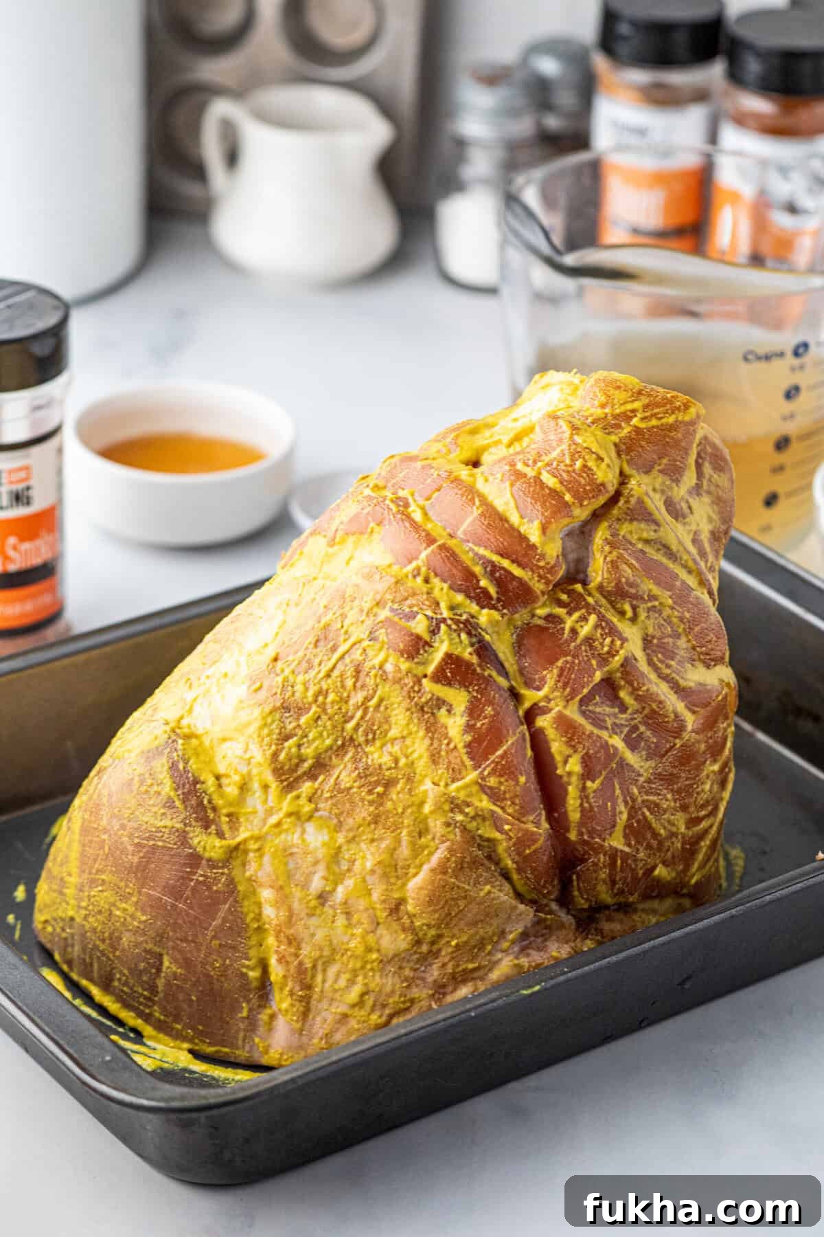 Lathering whole picnic ham with yellow mustard prior to seasoning in shallow baking pan