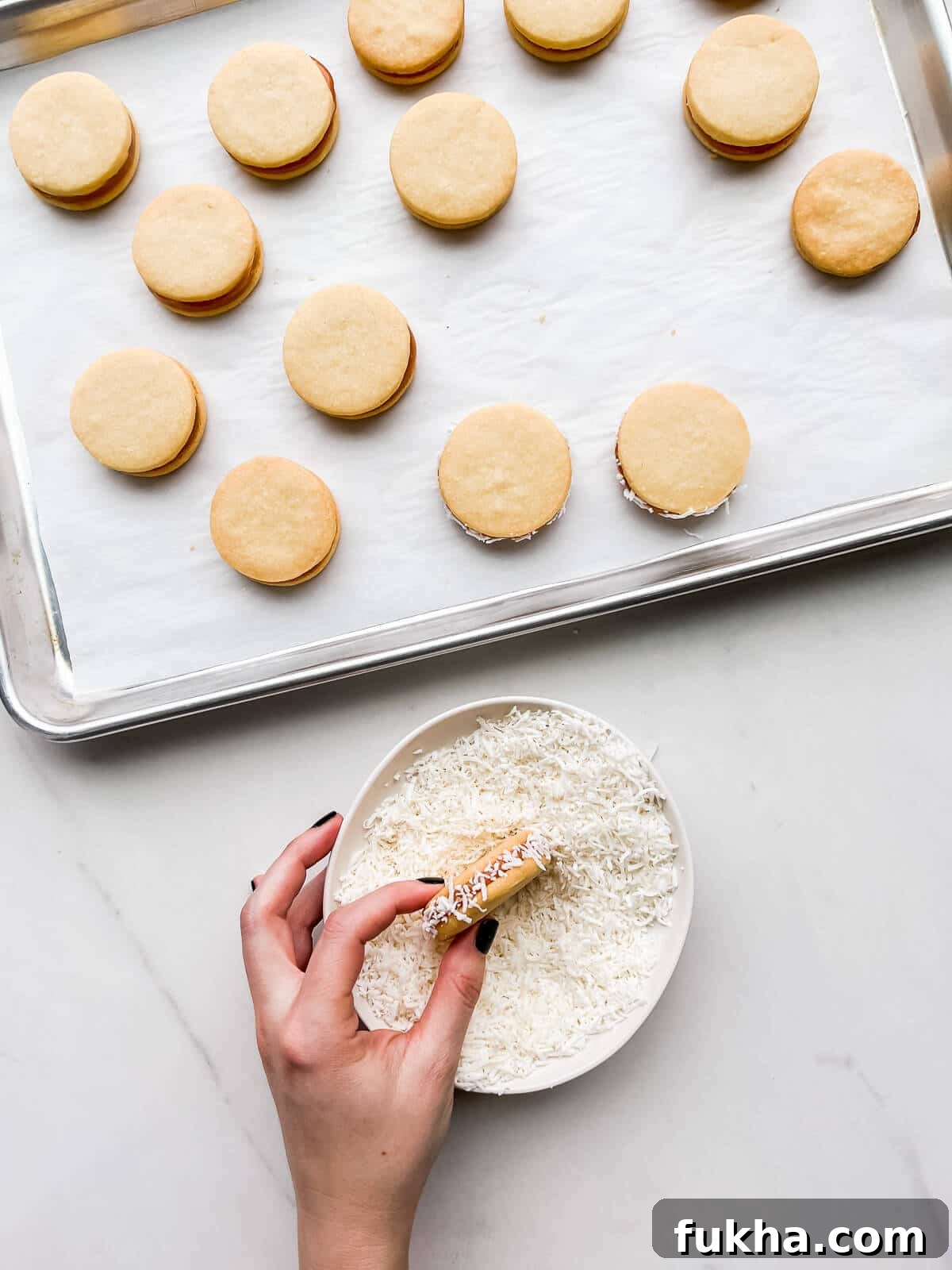 Classic Argentinian Alfajores Recipe with Dulce de Leche 10 Rolling alfajores cookies in a bowl of coconut to coat the edges.