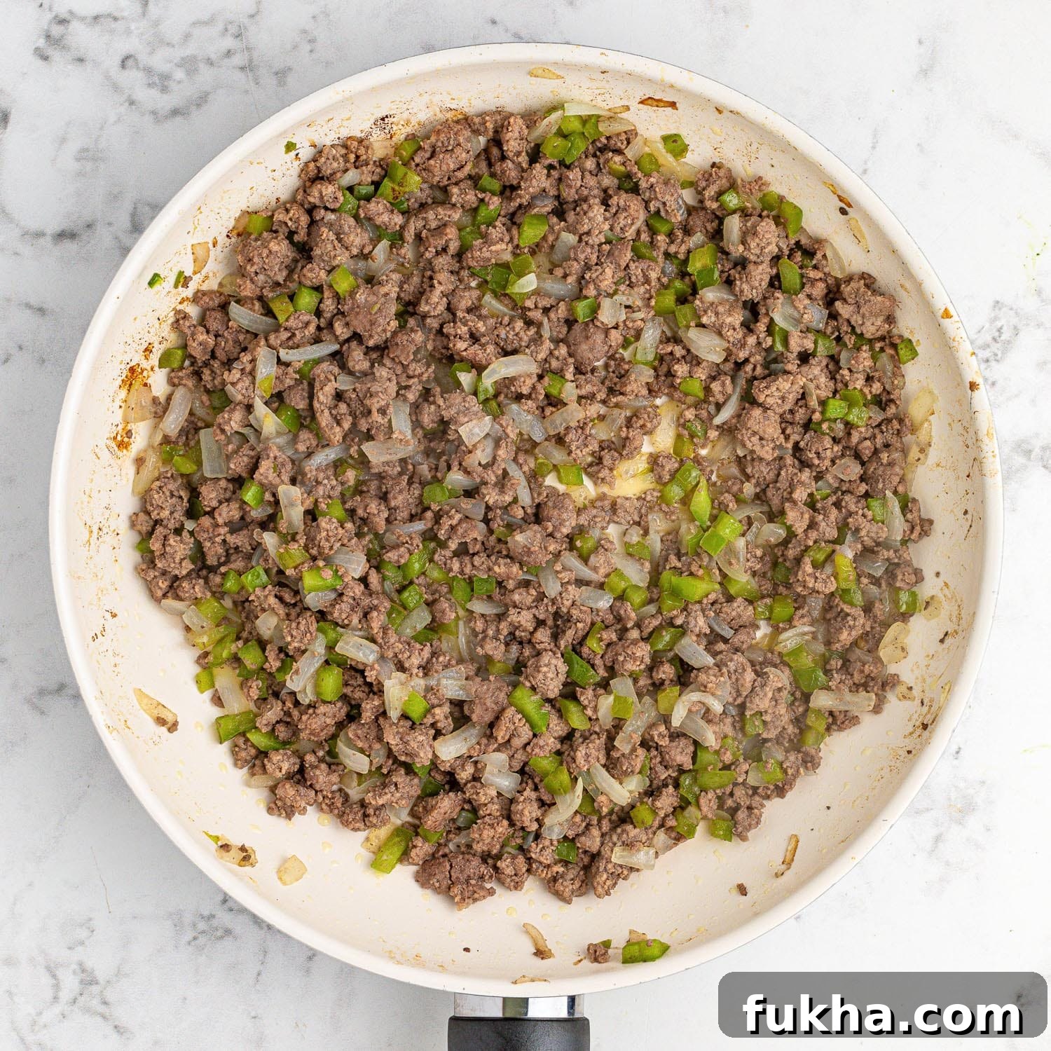 Cooked ground beef, onion and pepper in a white pan