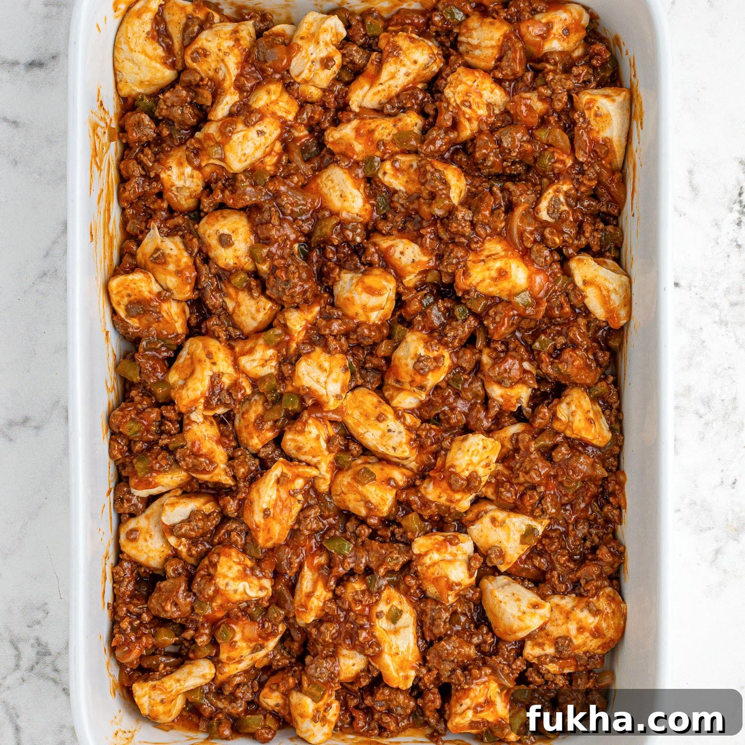 Sloppy joe meat sauce mixed with biscuit dough in a casserole dish before baking