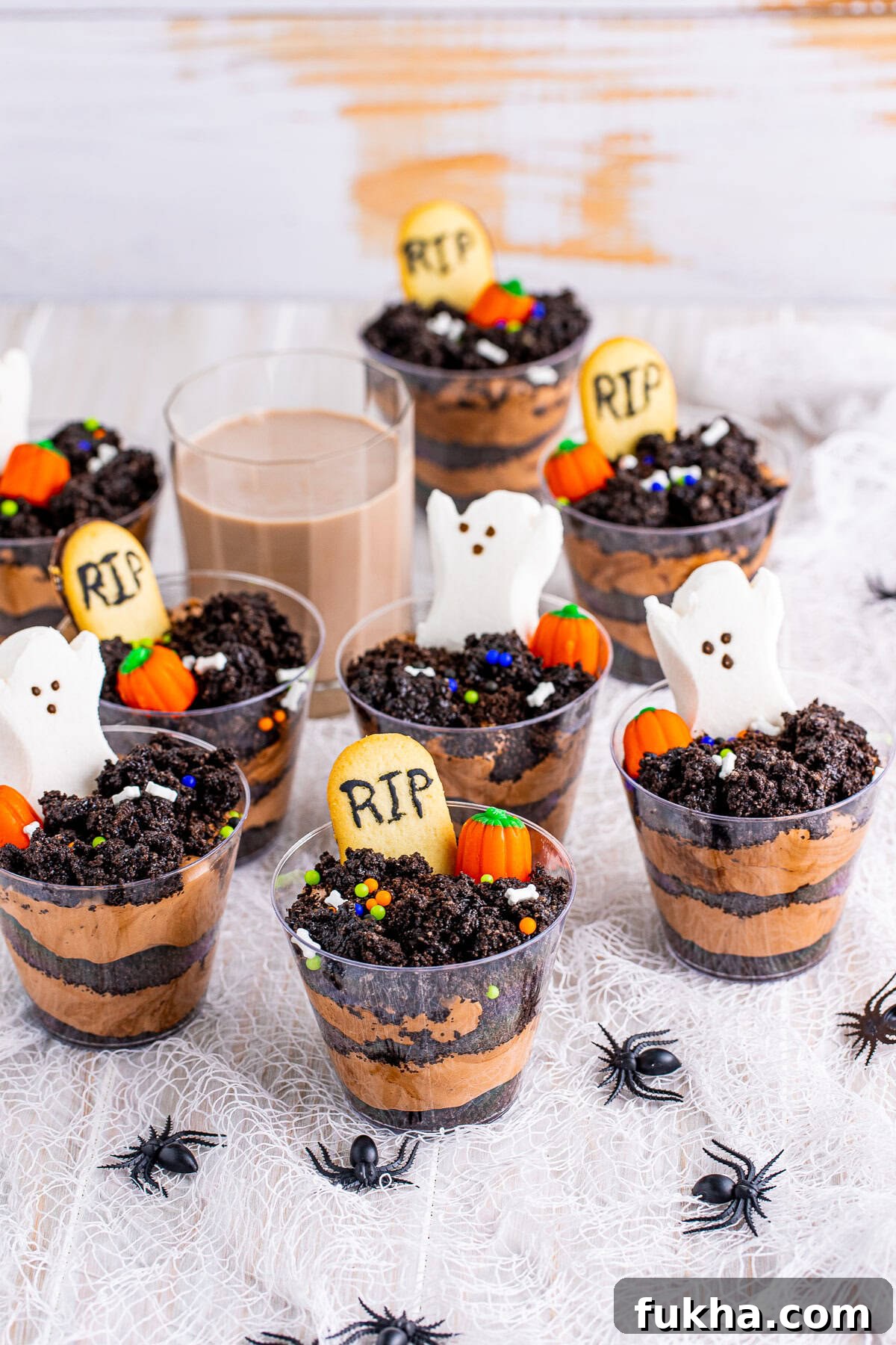 Graveyard Dirt Cups Recipe for Halloween 6 Dirt Cups spread out over a white linen with chocolate milk in background.