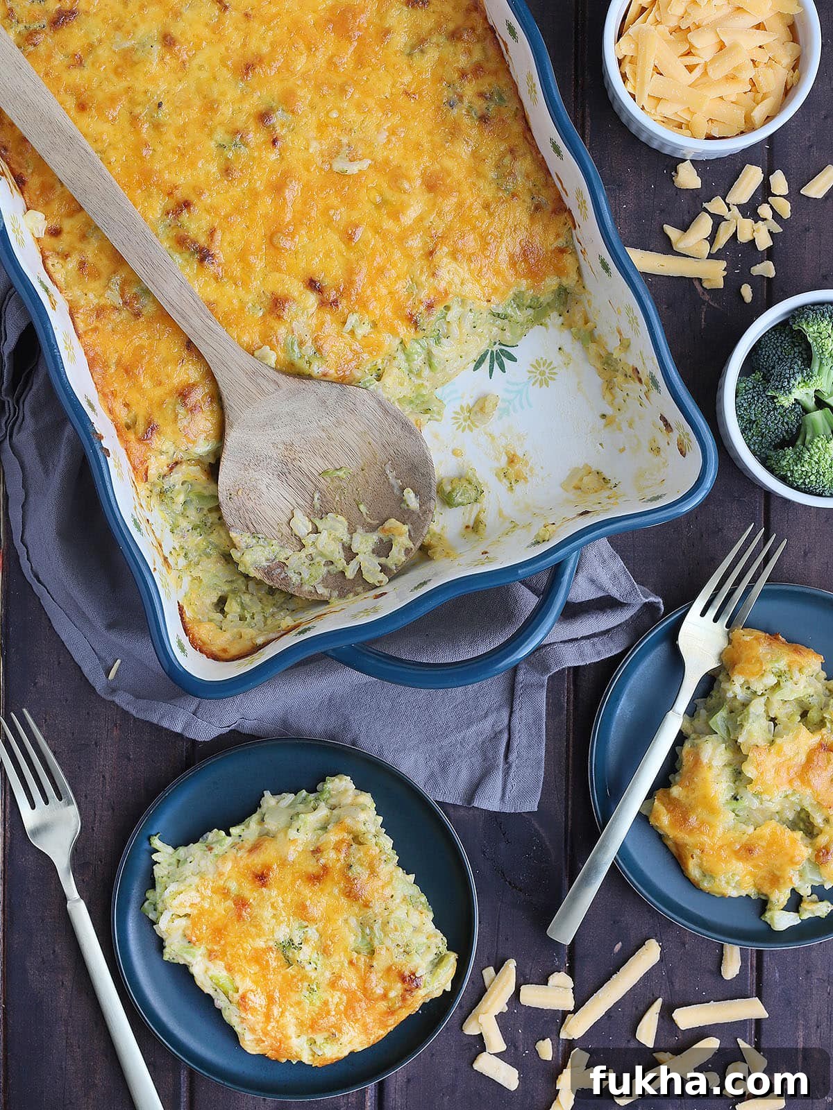 Creamy Broccoli Cheese Casserole 11 wooden serving spoon laid across the casserole dish with servings of cheesy broccoli casserole on the side